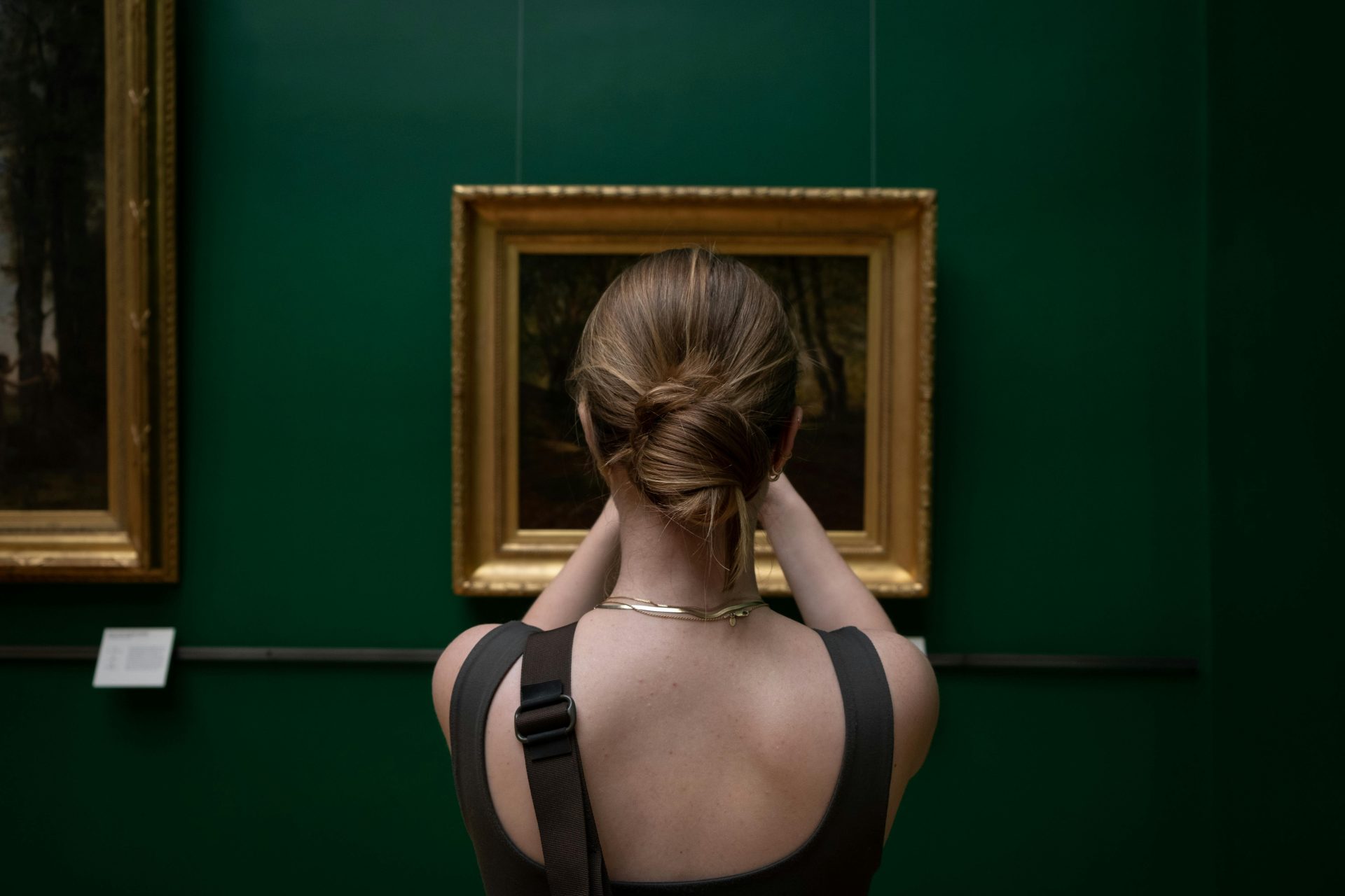 Vista posterior de una mujer fotografiando un cuadro en una galería de arte.